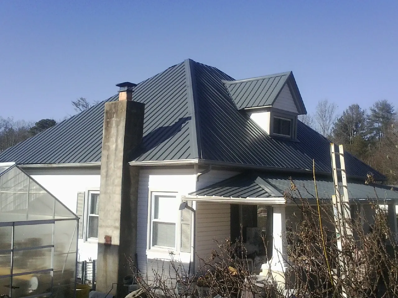 Dark blue standing seam metal roof on a white farmhouse with dormer — Slate & Tile Roof Repair by Roofing Brothers in Lynn Center