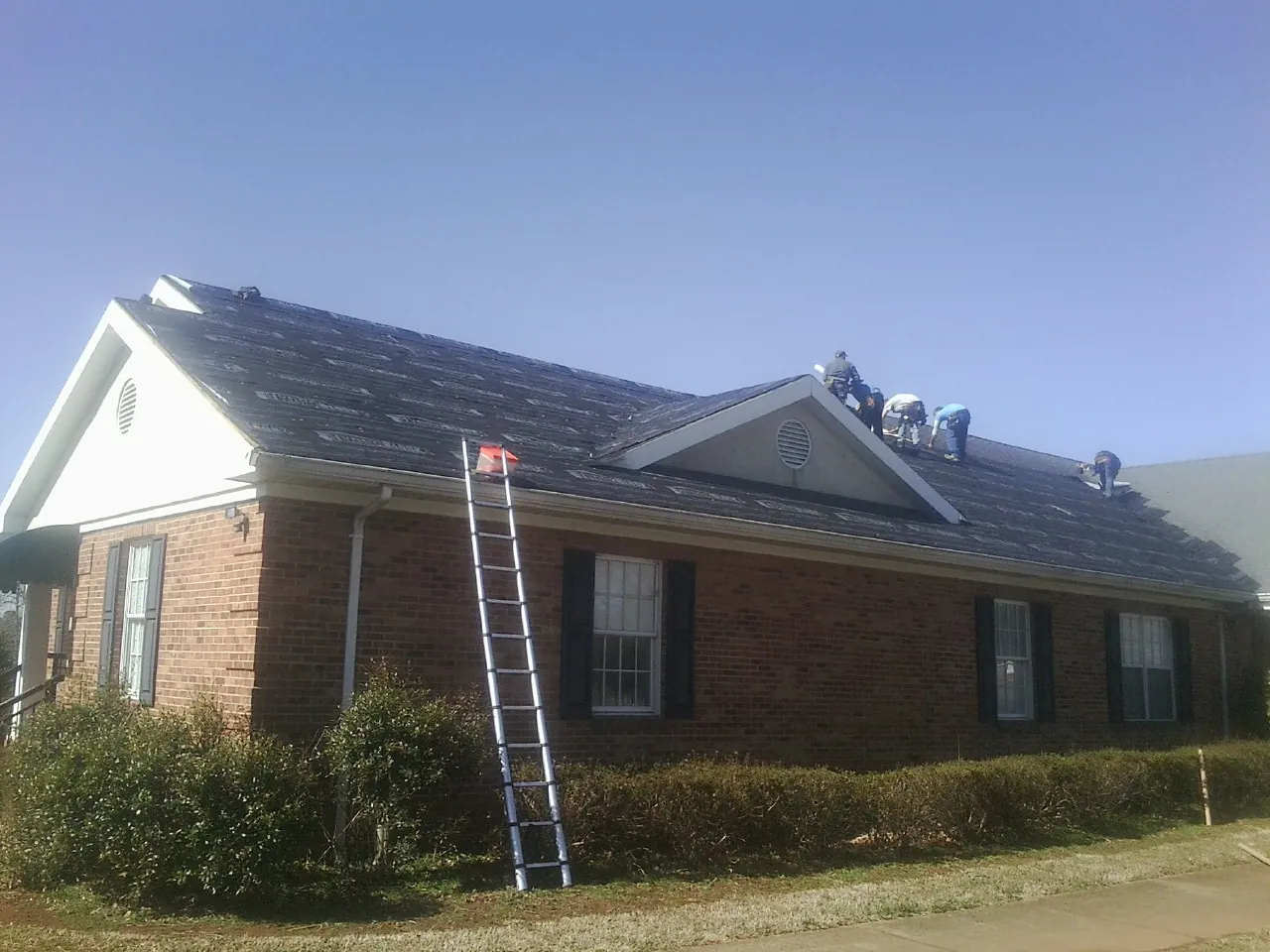 Crew tearing shingles off a brick ranch roof with a ladder set — Emergency Roof Repair work by our crew in Lynn Center