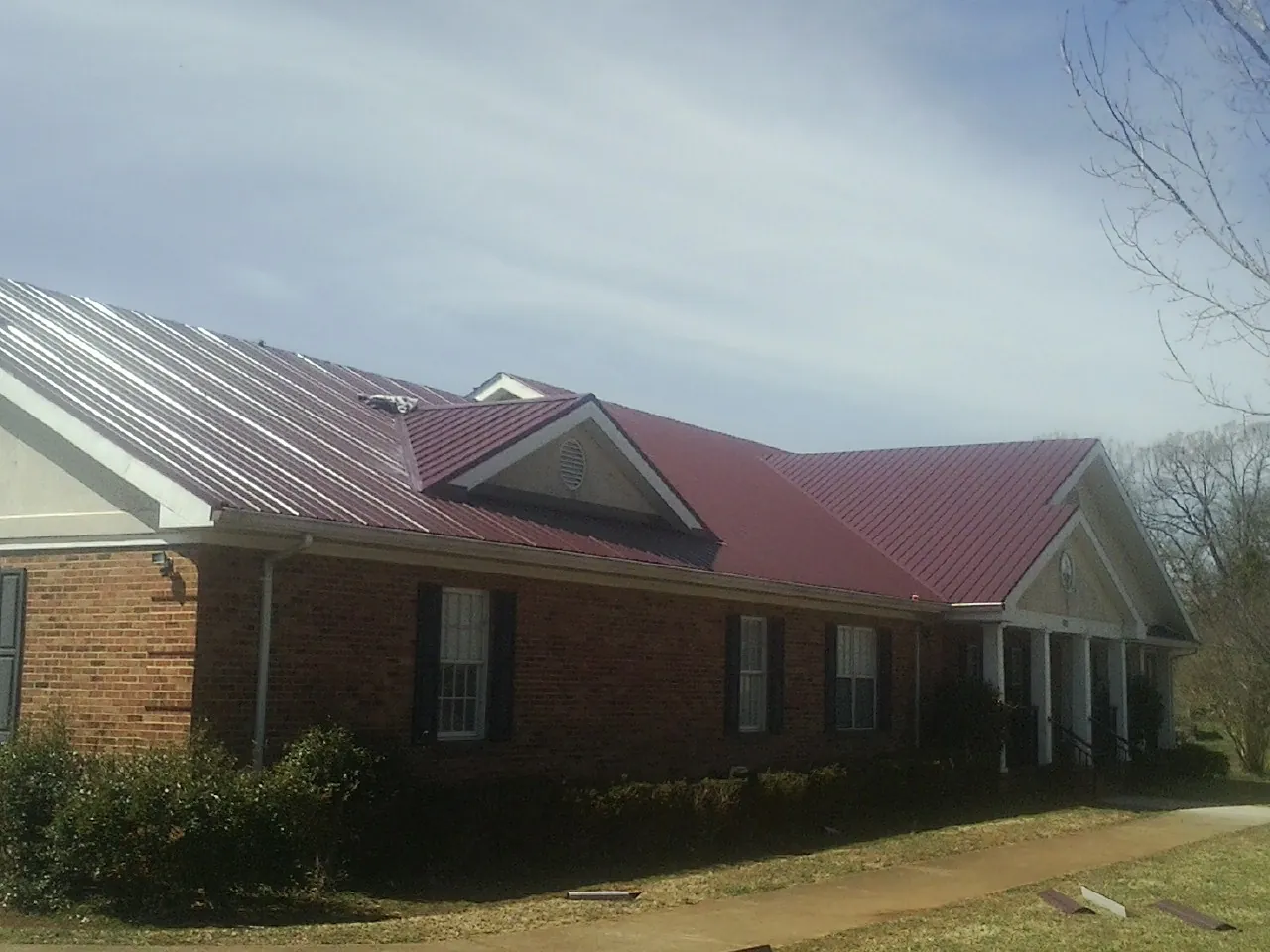 Red metal roof with gabled entries on a long brick building, from a Hail Damage Roof Repair job in Lynn Center