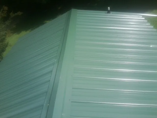 New green metal panels meeting at the ridge of a roof — Flat Roof Repair work by our crew in Lynn Center