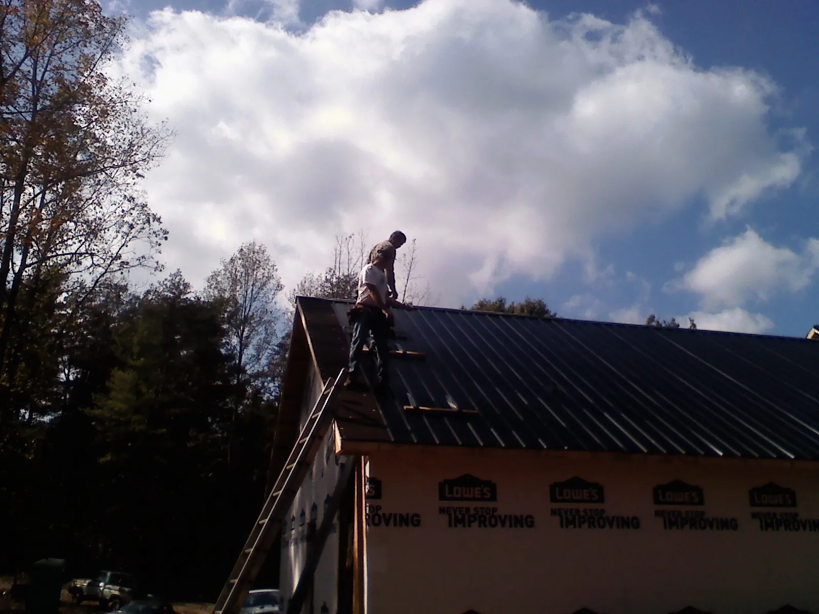 Roofer fastening dark metal panels high against a cloudy sky, from a Roof Inspection job in Lynn Center