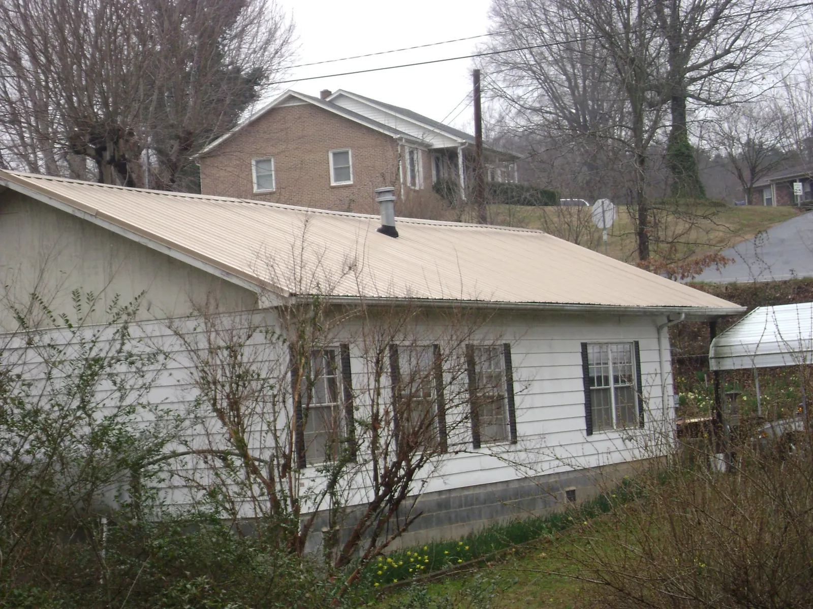 Tan metal roof on a white sided house set into a hillside — Commercial Roofing by Roofing Brothers in Lynn Center