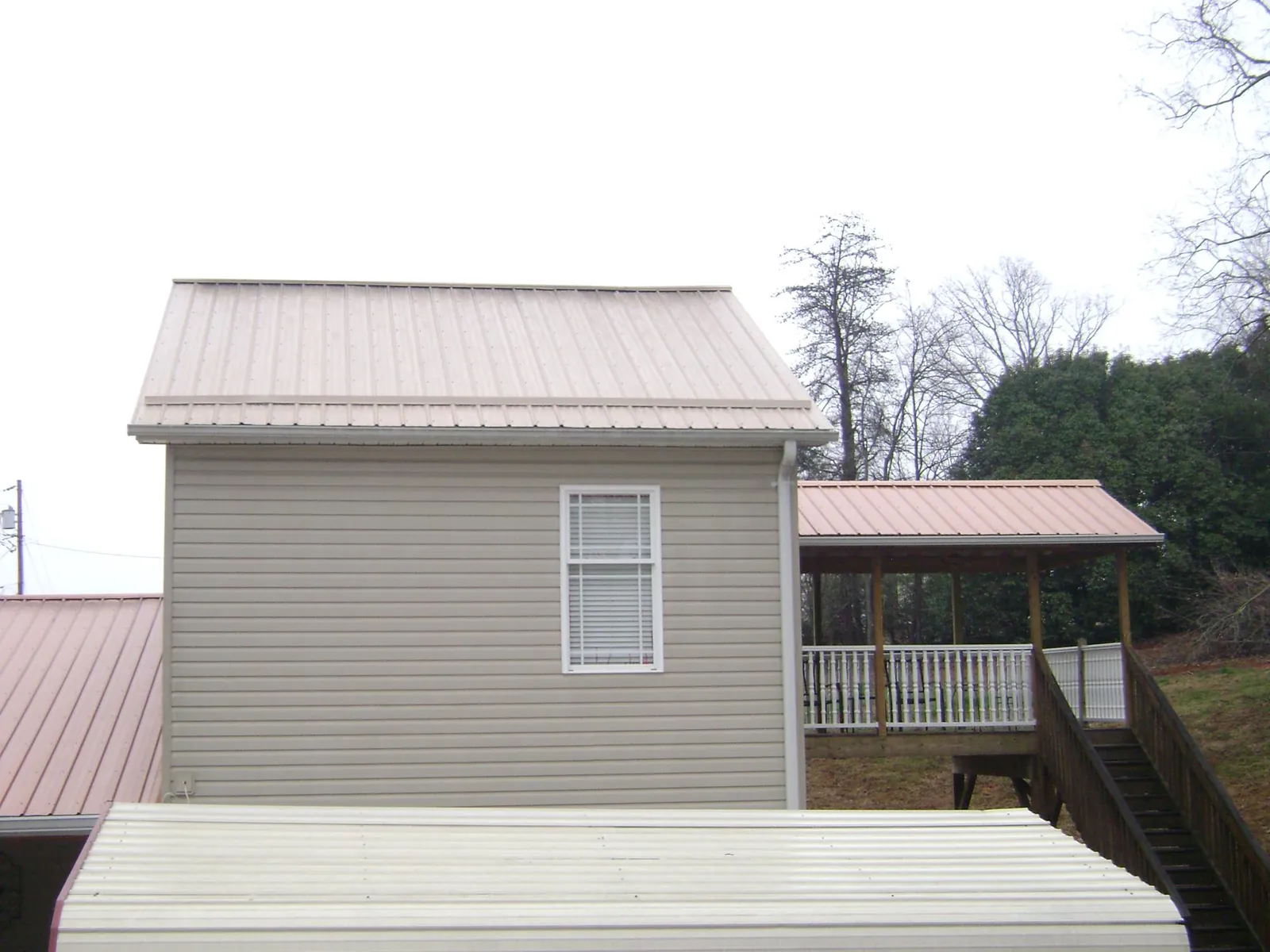 Tan metal roofs on a two story addition and attached porch, from a Roof Replacement job in Lynn Center